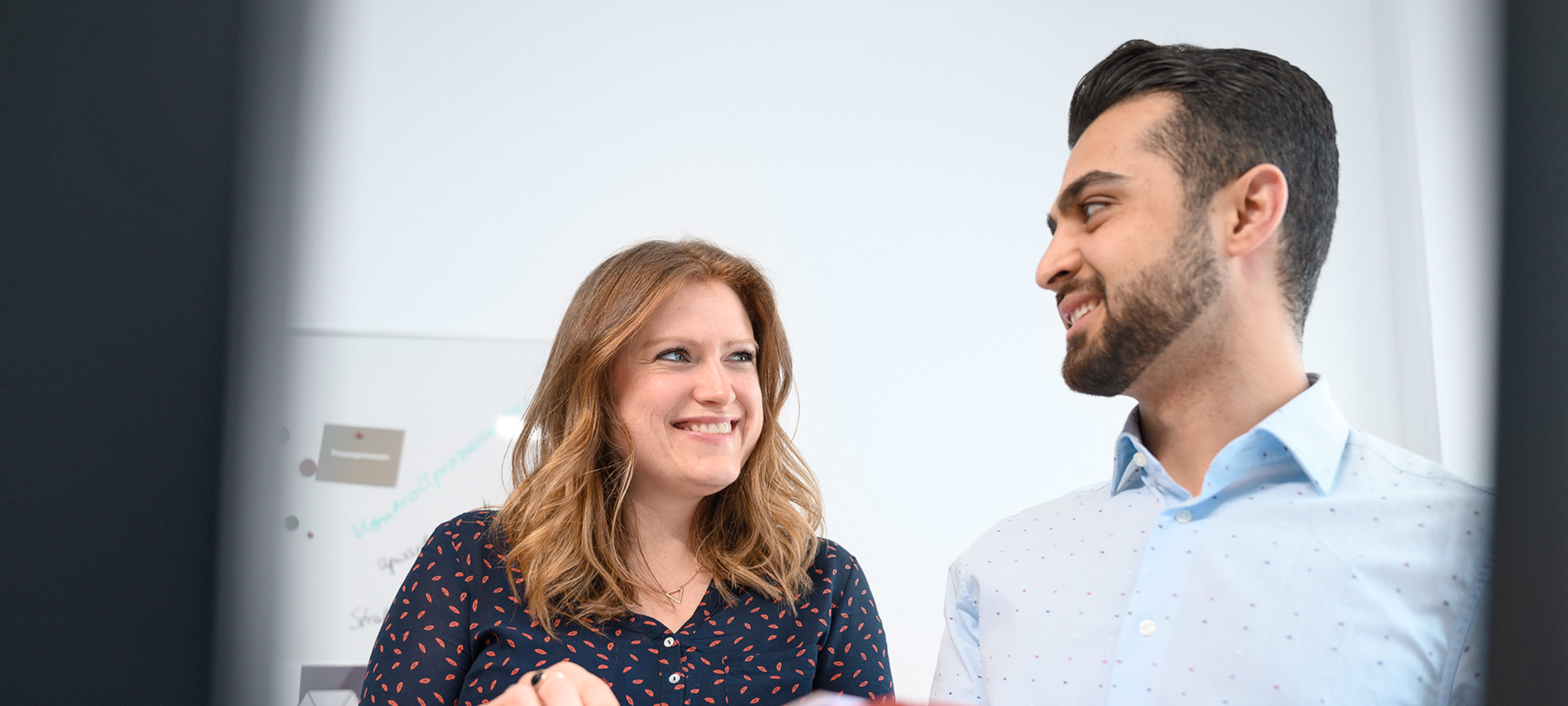 Zwei Mitarbeiter halten einen Ordner in der Hand und schauen sich an.